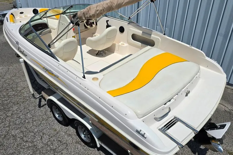 Slide: The Image of 2002 Rinker 212 Captiva BR boat with yellow accents, parked on a trailer. - 2