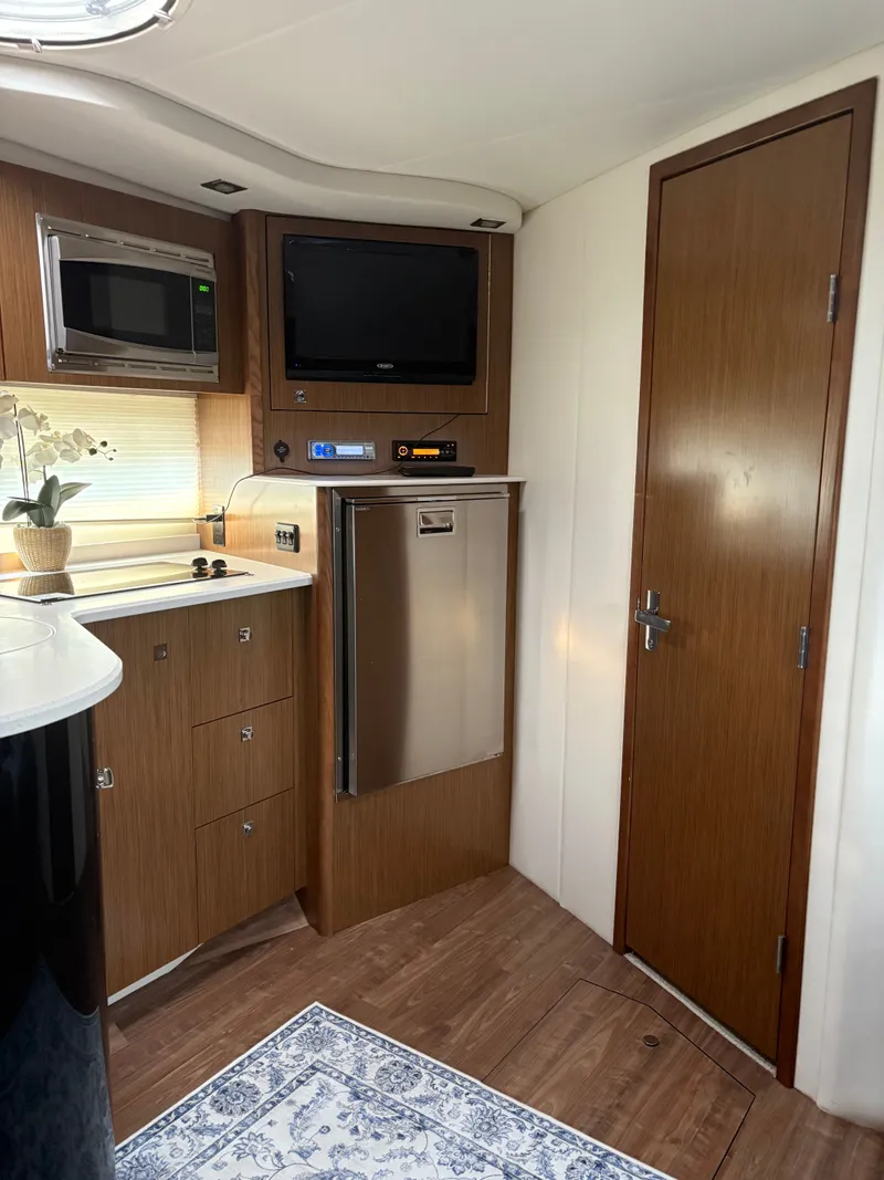 Slide: The Image of 2017 Cruisers Yachts 380 Express interior with kitchenette, microwave, TV, and wooden cabinetry. - 23