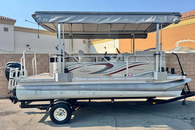 The Image of 2016 Apex Qwest 7518 LS pontoon boat on trailer, featuring canopy and Mercury outboard motor. - 0