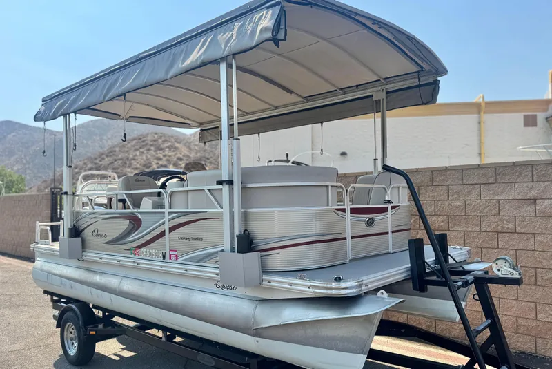 Slide: The Image of 2016 Apex Qwest 7518 LS pontoon boat with canopy on trailer, parked outdoors. - 1
