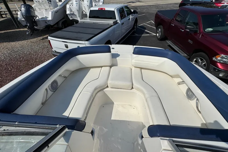 Slide: The Image of 2015 Bayliner 190 Deck Boat interior with white and blue seating, parked near trucks. - 14