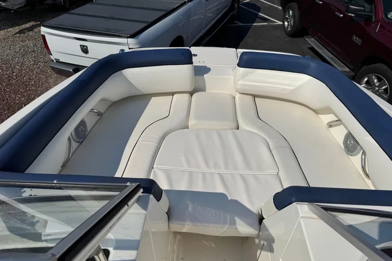 Slide: The Image of 2015 Bayliner 190 Deck Boat interior with white and blue seating, parked near trucks. - 17