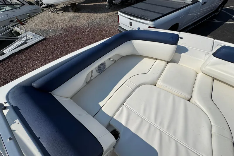 Slide: The Image of 2015 Bayliner 190 Deck Boat interior with white and blue seating, parked near other boats. - 18