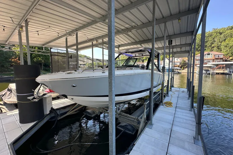 Slide: The Image of 2020 Chaparral 300 OSX boat docked under a covered marina on a sunny day. - 14