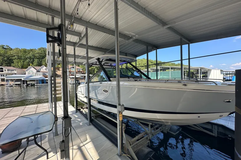 Slide: The Image of 2020 Chaparral 300 OSX boat docked under a covered marina with scenic waterfront view. - 16