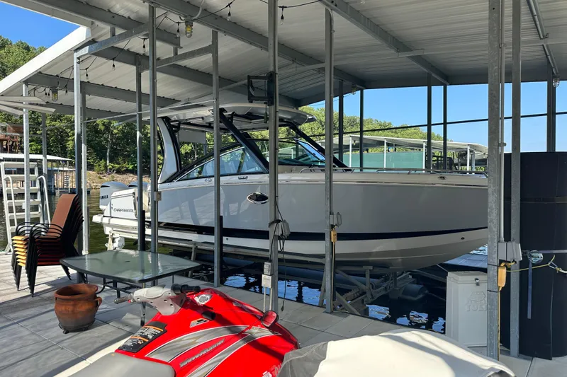 Slide: The Image of 2020 Chaparral 300 OSX boat docked under a covered marina with a red jet ski nearby. - 2