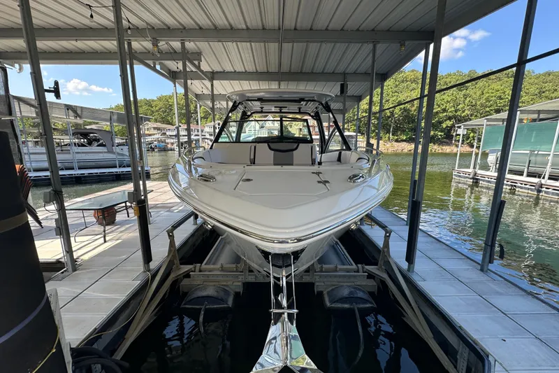 Slide: The Image of 2020 Chaparral 300 OSX boat docked in a covered marina, surrounded by water and trees. - 7