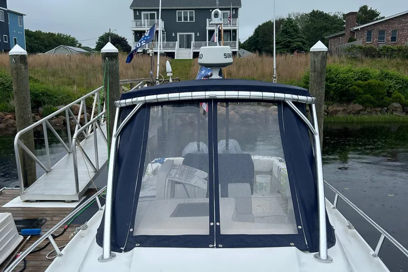 Slide: The Image of 2003 Intrepid 310 Walkaround boat docked, featuring a covered cockpit and nearby residential backdrop. - 3
