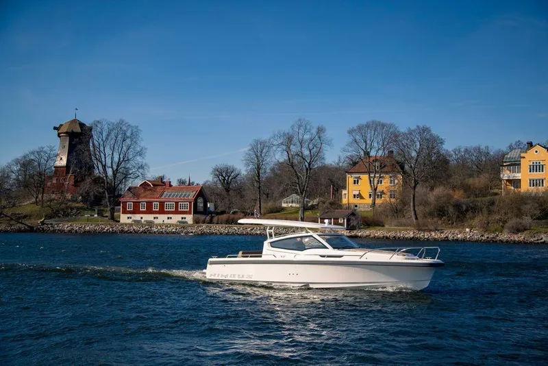 Slide: The Image of 2023 Nimbus W9 boat cruising on a scenic river with historic buildings in the background. - 12