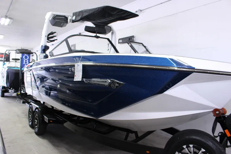 Slide: The Image of 2024 Nautique G25 boat in showroom, blue and white design, on trailer. - 0