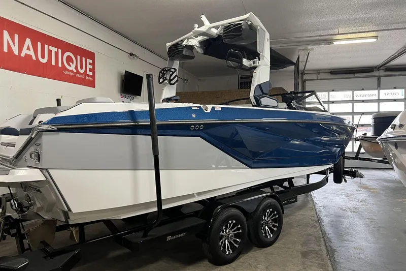 Slide: The Image of 2024 Nautique G25 boat in showroom, blue and white design, on trailer. - 1