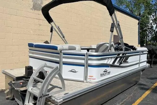 Slide: The Image of 2025 SunCatcher Select 18C pontoon boat with canopy, parked near a beige wall. - 1