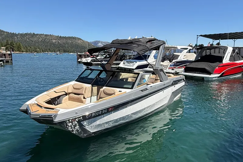 Slide: The Image of 2025 MasterCraft XStar 23 boat docked on a clear lake with scenic mountain backdrop. - 2