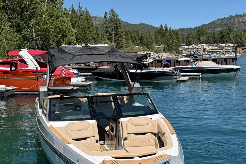 Slide: The Image of 2025 MasterCraft XStar 23 boat docked on a scenic lake with surrounding trees and other boats. - 5