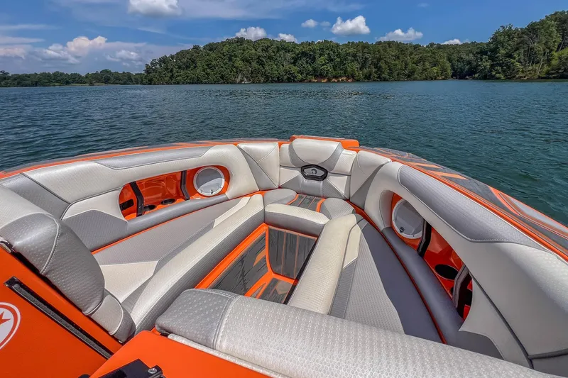 Slide: The Image of 2022 Centurion Ri245 boat interior with orange and gray seating on a serene lake. - 16