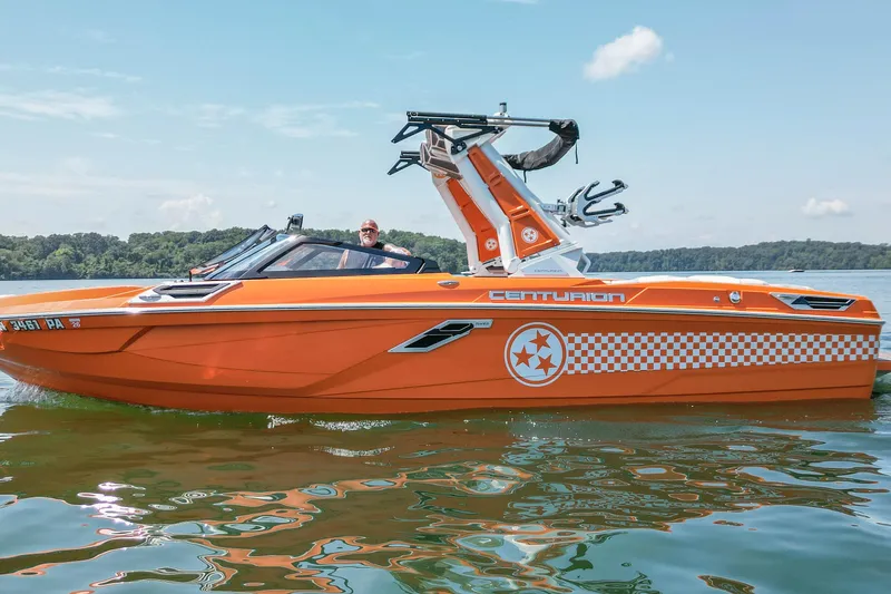 Slide: The Image of 2022 Centurion Ri245 boat in vibrant orange on a calm lake. - 2