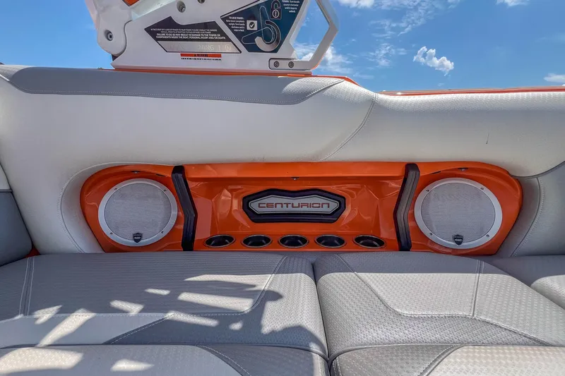 Slide: The Image of 2022 Centurion Ri245 boat interior with orange speaker panel and gray seating under blue sky. - 26