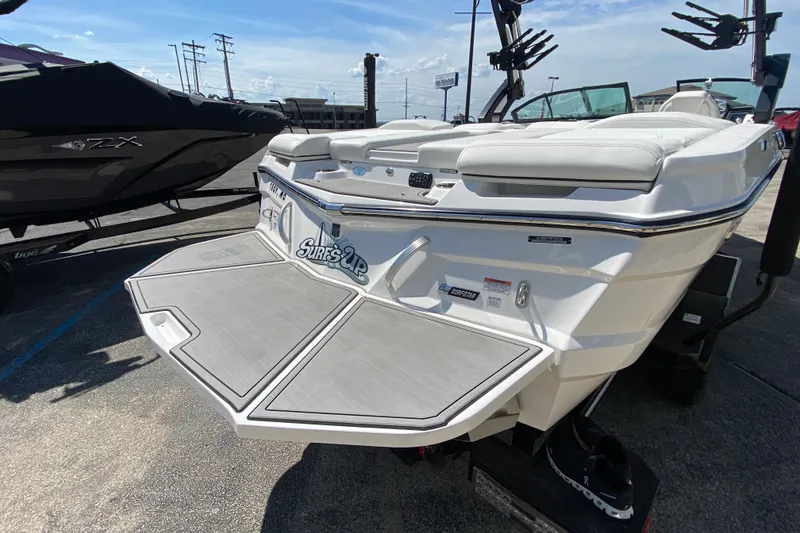 Slide: The Image of 2022 MasterCraft XT25 boat with swim platform, "Surf's Up" decal, parked outdoors. - 6
