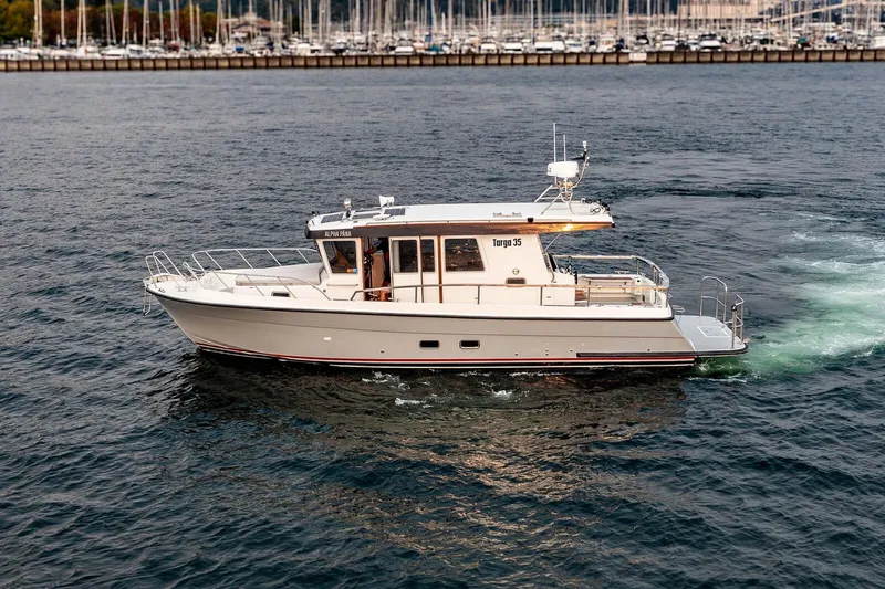 The Image of 2019 Targa 35 boat cruising on water near marina with numerous docked sailboats. - 0