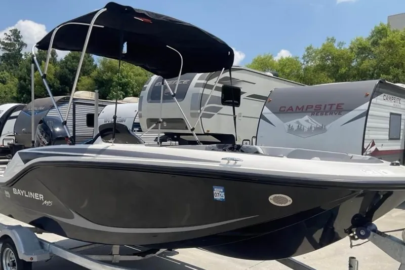 Slide: The Image of 2024 Bayliner M15 boat with canopy, parked near RVs at a campsite. - 1