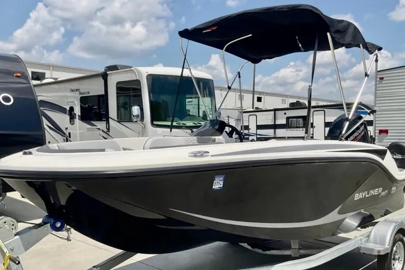 Slide: The Image of 2024 Bayliner M15 boat with canopy on trailer, parked near RVs under a cloudy sky. - 2