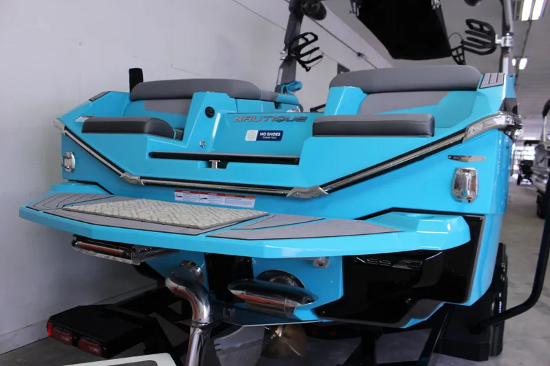 Slide: The Image of 2023 Nautique G25 boat in vibrant blue, rear view in showroom. - 3