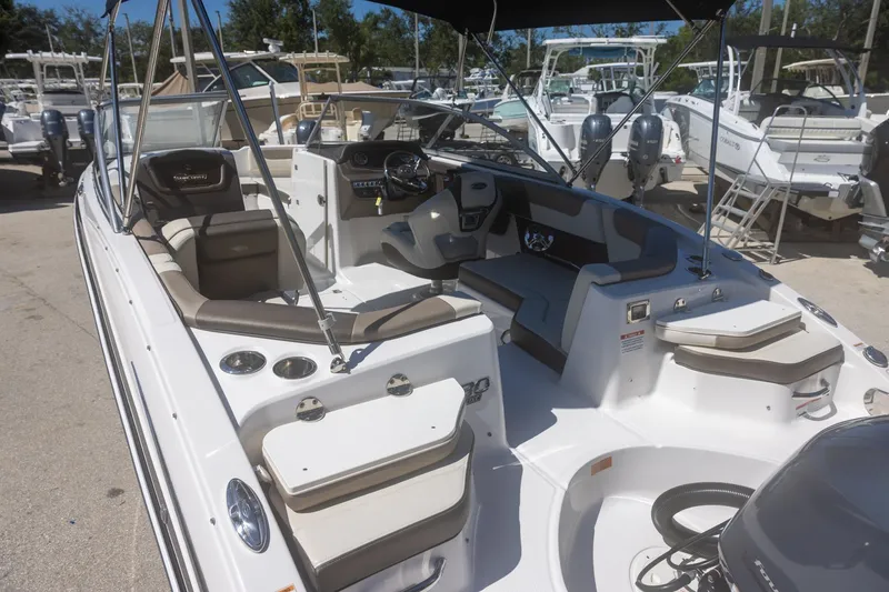 Slide: The Image of 2019 Chaparral 230 Suncoast boat interior with seating and controls, docked among other boats. - 7