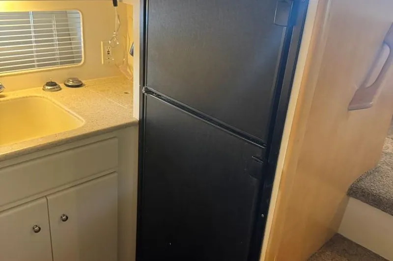 Slide: The Image of 1998 Carver 405 Motor Yacht kitchen with black fridge, sink, and cabinets. - 41