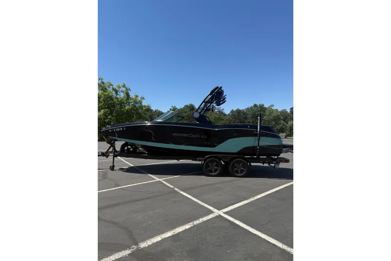 Slide: The Image of 2025 MasterCraft NXT22 boat on trailer in parking lot under clear blue sky. - 0