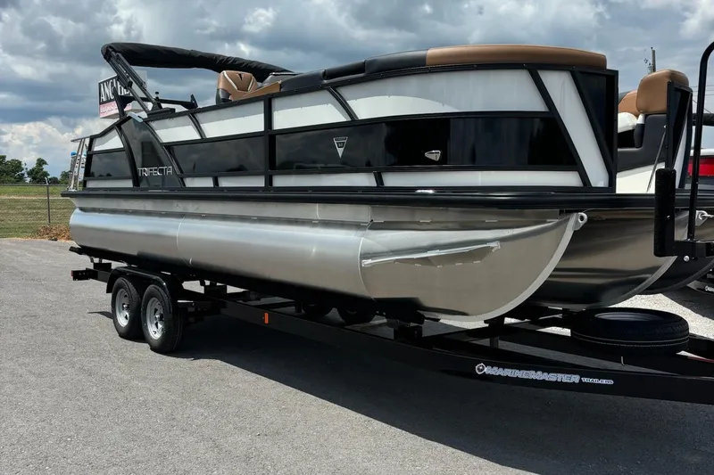 Slide: The Image of 2026 Trifecta 23 ULE SS pontoon boat on trailer, parked outdoors under cloudy sky. - 1