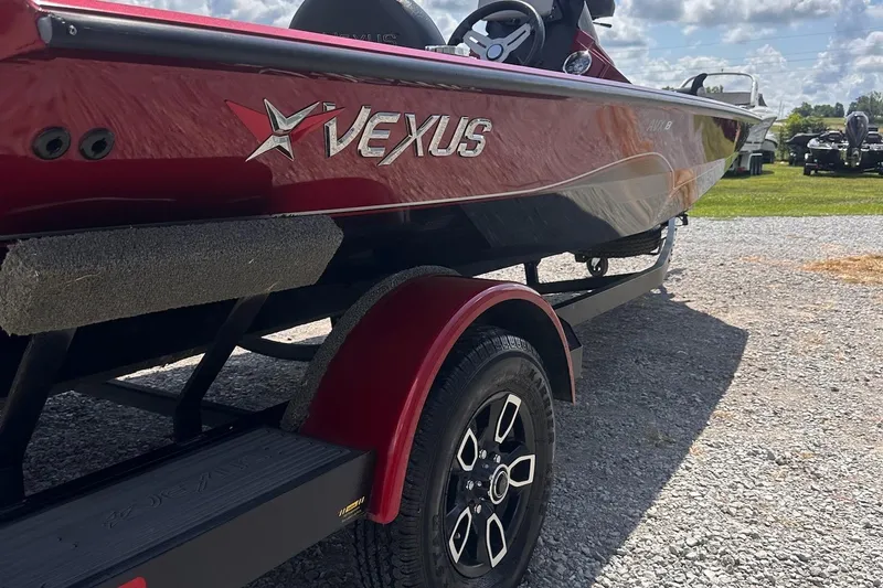 Slide: The Image of 2021 Vexus AVX181 boat on trailer, red and black design, parked outdoors. - 2