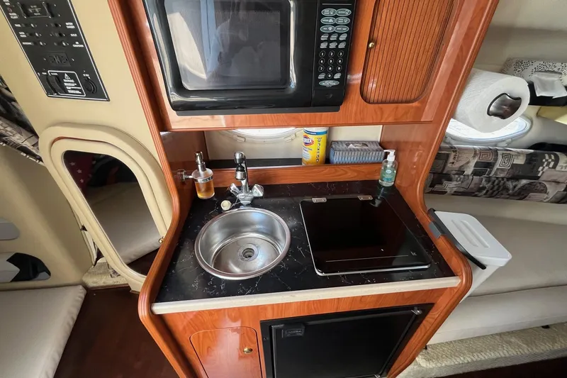 Slide: The Image of 2004 Rinker Fiesta Vee 270 cabin with kitchenette, featuring microwave, sink, and compact fridge. - 12