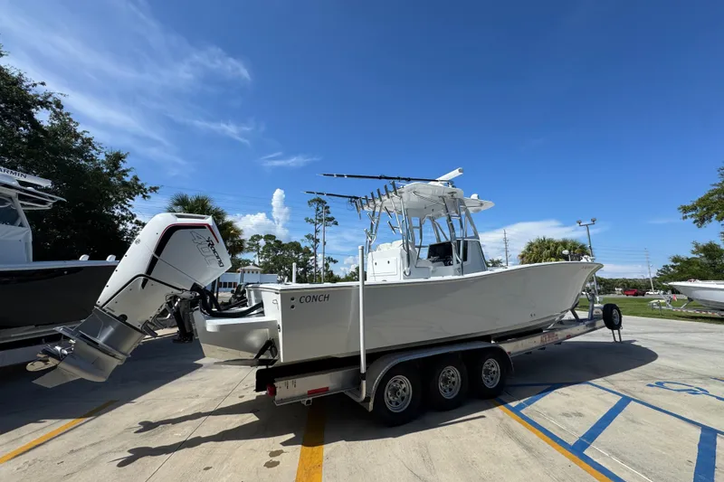 Slide: The Image of 2025 Conch 33 boat on trailer, featuring powerful outboard motor, parked outdoors under clear sky. - 13