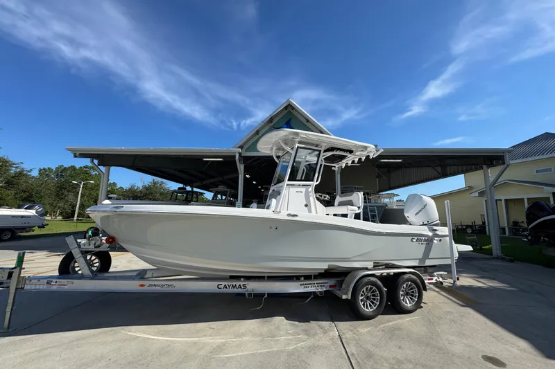 Slide: The Image of 2026 Caymas 24 HB boat on trailer under blue sky, parked near a covered area. - 2