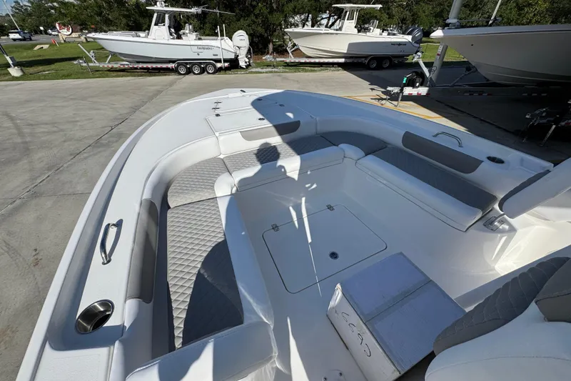 Slide: The Image of 2026 Caymas 24 HB boat interior with cushioned seating and storage, parked outdoors. - 20