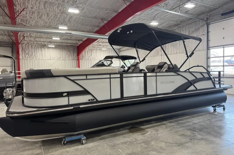 Slide: The Image of 2026 Sylvan L-5 pontoon boat in showroom, featuring sleek design and black canopy. - 2