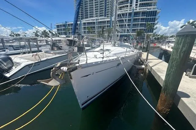 Slide: The Image of 2005 Jeanneau Deck Salon 43 yacht docked at marina with modern buildings in background. - 2
