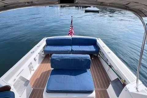 Slide: The Image of 2004 Hunt Yachts Surfhunter 25 with blue seating, American flag, and wooden deck on calm water. - 17