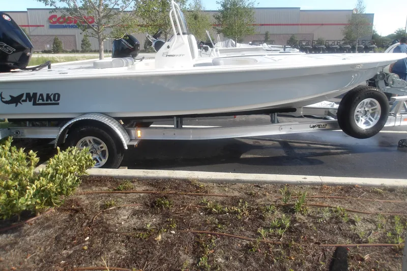 Slide: The Image of 2026 Mako 18 Pro Skiff boat on trailer, parked outdoors near a store. - 2