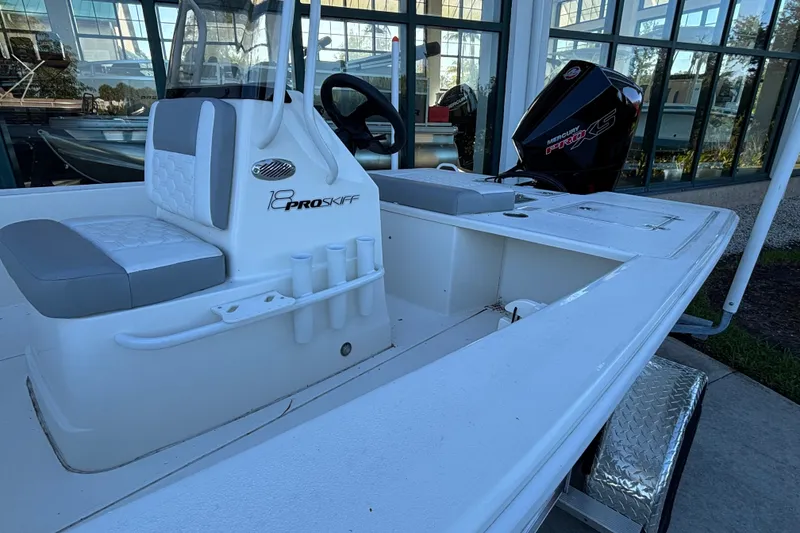Slide: The Image of 2026 Mako 18 Pro Skiff boat with Mercury engine, docked near a glass building. - 4