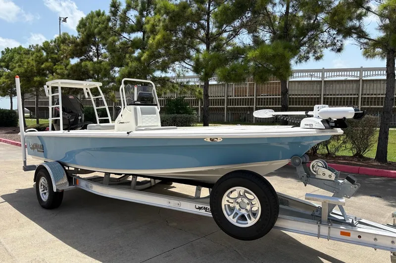 Slide: The Image of 2026 Mako 18 Pro Skiff boat on trailer, parked outdoors near trees. - 2