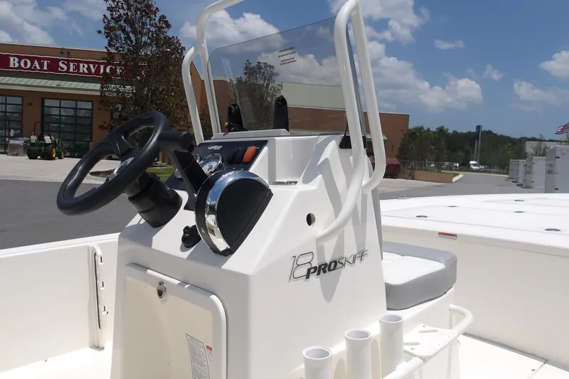 Slide: The Image of 2026 Mako 18 Pro Skiff boat console with steering wheel and controls, outdoors near service center. - 18