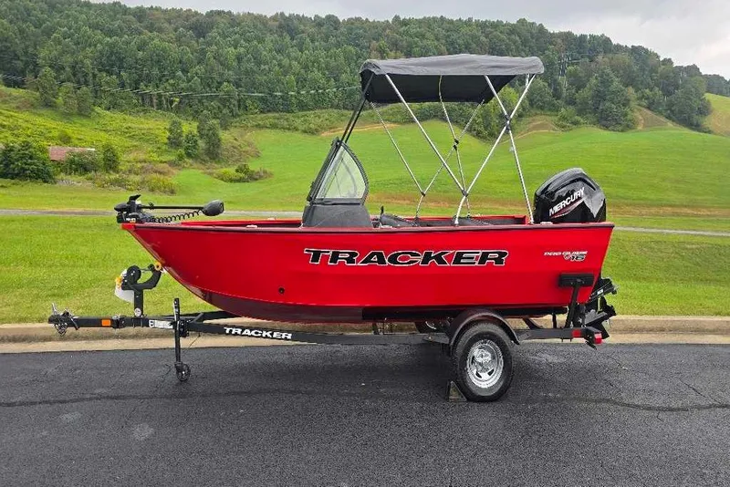 The Image of 2026 Tracker Pro Guide V-16 WT boat on trailer, red with canopy, scenic background. - 0