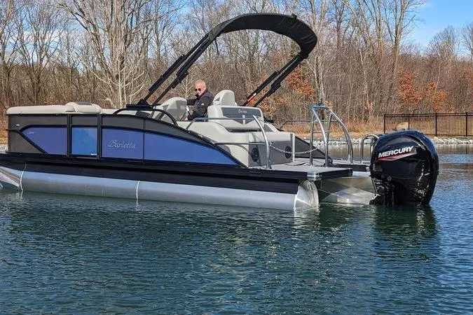 Slide: The Image of 2024 Barletta Cabrio 20UC pontoon boat on a calm lake with Mercury outboard motor. - 2