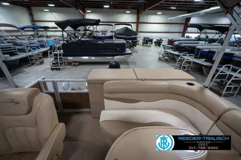 Slide: The Image of 2017 Bennington 18 SLX pontoon boat interior in showroom with tan seating and multiple boats. - 17