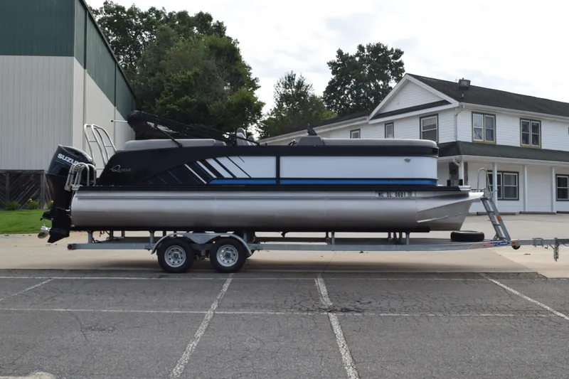Slide: The Image of 2025 Qwest L-Class 822 RLS pontoon boat on trailer, parked near buildings. - 2