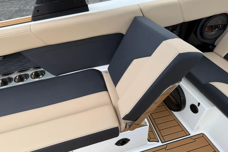 Slide: The Image of 2025 MasterCraft X24 boat interior with beige and navy seating, cup holders, and teak flooring. - 13