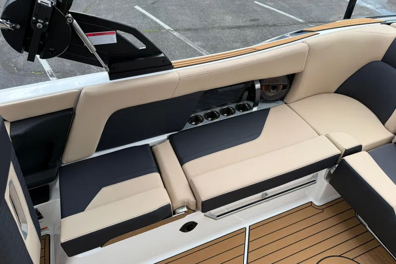 Slide: The Image of 2025 MasterCraft X24 boat interior with beige and black seating, cup holders, and teak flooring. - 14