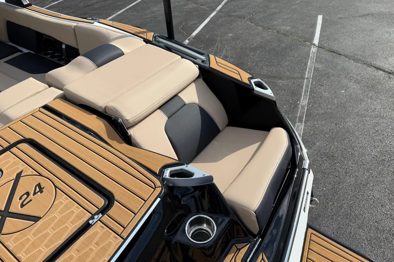 Slide: The Image of 2025 MasterCraft X24 boat interior with beige and black seating, cup holder, and teak flooring. - 29