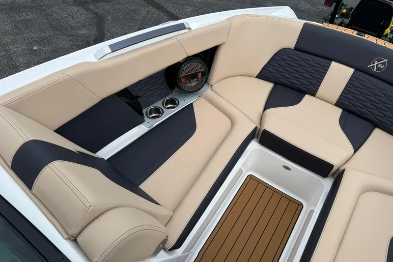 Slide: The Image of 2025 MasterCraft X24 boat interior with beige and navy seating, cup holders, and speaker. - 9